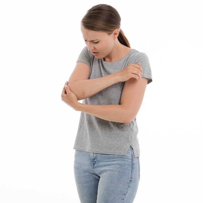 Kvinna som håller i sin armbåge och visar att hon har ont. Illustrerar smärtan man kan känna vid padelarmbåge (tennisarmbåge)